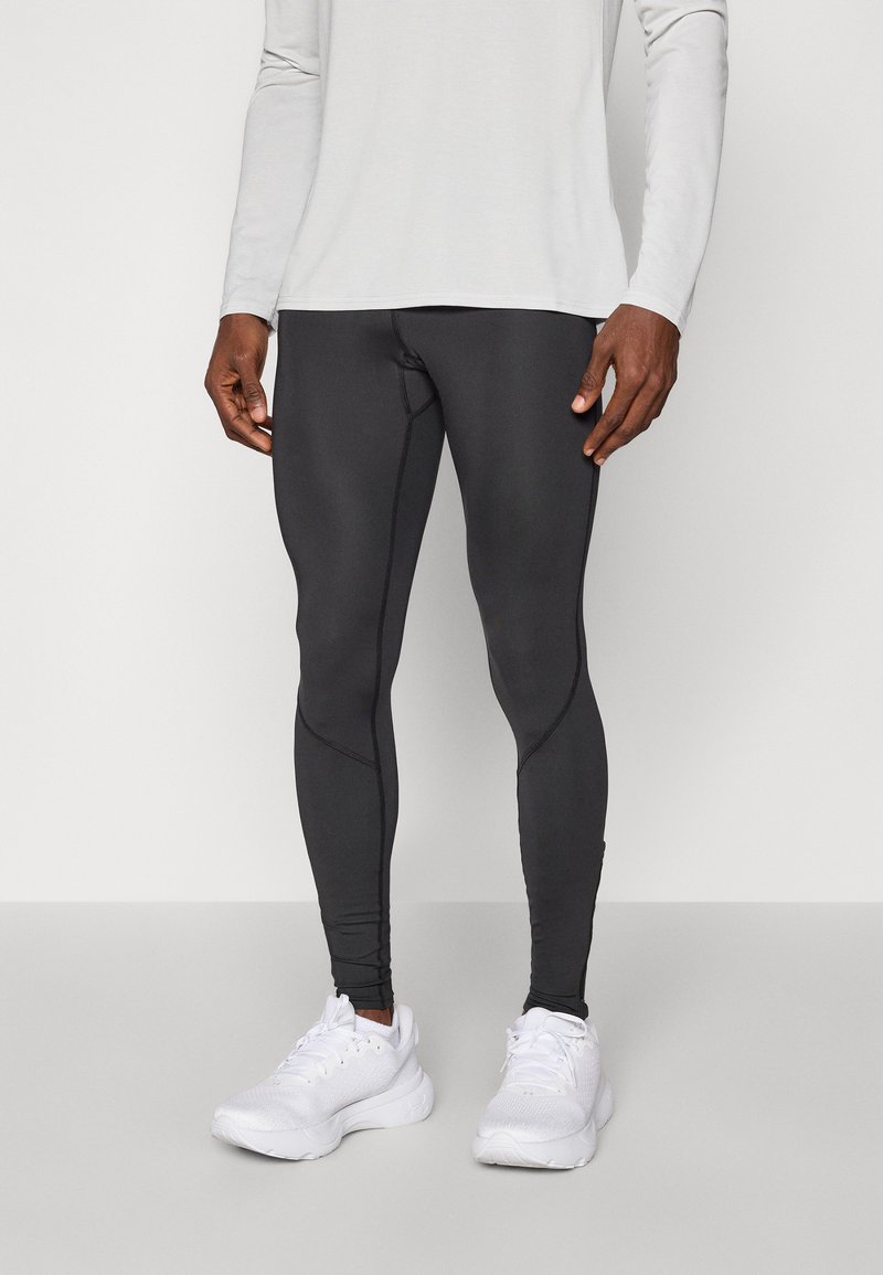 Leggings sportivi neri con un design aderente, caratterizzati da dettagli in cucitura e una superficie liscia, abbinati a scarpe da corsa bianche.