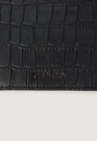 Fekete bőr pénztárca krokodilbőr mintával, diszkrét varrásokkal, és a Calvin Klein logo benyomva az alján.