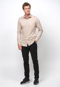 Beige Langarmhemd mit spitzem Kragen und Knopfleiste, kombiniert mit schwarzen Slim-Fit-Hosen und schwarzen Sneakers. Glatte Textur, taillierte Passform.