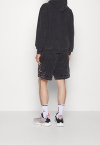 Felpa nera strappata con una vestibilità comoda, abbinata a pantaloni corti neri coordinati. Sneakers grigie con accenti rosa e calzini bianchi con logo.