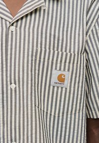 Ριγέ βαμβακερό πουκάμισο με κοντό μανίκι σε μπεζ και γκρι χρώμα, με τσέπη-μπαλαντέρ και ετικέτα με λογότυπο, λευκά κουμπιά και γιακά τύπου κάμπ.