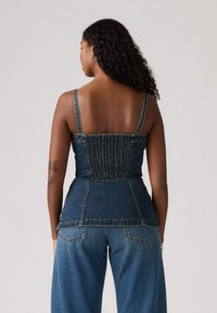 Top en denim avec peplum, smocks élastiques au dos, bretelles réglables et une silhouette légèrement évasée. Couleur bleu foncé avec une finition lisse.