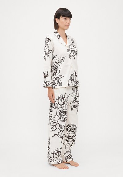Set de pijama din satin alb cu modele florale negre, inclusiv trandafiri și frunze, format dintr-o cămașă cu guler și nasturi și pantaloni evazați.