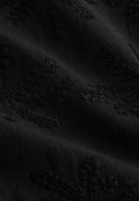Tissu noir à la texture douce, présentant une broderie ton sur ton complexe de motifs de feuilles sur toute la surface. L'apparence froissée ajoute de la profondeur.