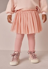 Jupe plissée rose avec une ceinture élastique, associée à des leggings roses côtelés et des chaussures montantes avec des lacets scintillants et des poignets à volants.