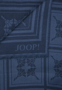 Navyblauwe jacquard sjaal met geometrische patronen en franjes, met een zichtbaar "JOOP!" logo in het ontwerp geweven.
