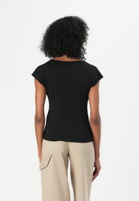 Top scurt negru cu guler rotund, mulat în talie. Stilizat cu pantaloni bej cu croi larg. Țesătură netedă și design simplu.