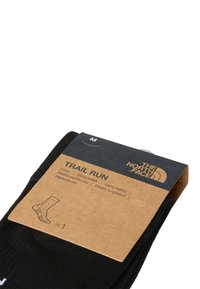 Calcetines de crew negros empaquetados con una etiqueta de cartón marrón. La etiqueta presenta el nombre del producto, el logotipo de la marca y una ilustración del diseño del calcetín.
