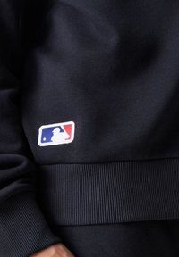 Felpa blu navy con orlo e polsini a coste, decorata con un logo MLB ricamato bianco, rosso e blu sul davanti.