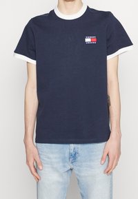 Marineblaue Baumwoll-T-Shirt mit weißem geripptem Kragen und Ärmelbündchen. Verfügt über ein kleines Marken-Patch mit rot-, weiß- und blau gestreiften Mustern.