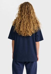 Marinblå bomullsoversized t-shirt med kortärmar. Slät textur och rak avslutning, sedd bakifrån.