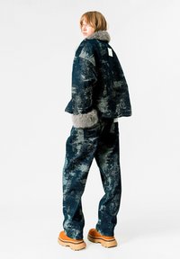 Conjunto de denim que incluye una chaqueta texturada de color azul oscuro con detalles en gris y puños de piel sintética, combinada con pantalones a juego y botas gruesas marrones.