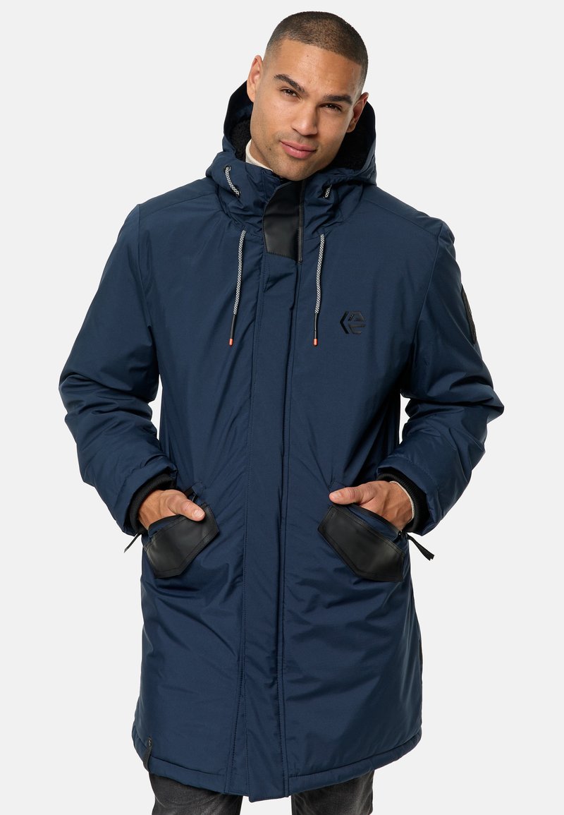 La chaqueta parka larga en color navy cuenta con un cierre frontal, una capucha ajustable, dos bolsillos con cremallera y detalles en cuero en los bolsillos y puños.