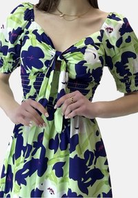 Grön och marinblå blommig klänning med korta puffärmar, detaljer med knytning framtill och smockad bodice; lättviktig tyg med en flödande silhuett.