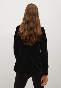 Czarna aksamitna marynarka o dopasowanym kroju, z wyciętymi klapami i pojedynczym rozcięciem z tyłu. Posiada rękawy zapinane na guziki.