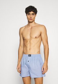Boxers rayés bleu et blanc en tissu léger, avec une taille élastique et un détail de bouton à l'avant, conçus pour le confort et l'ajustement.