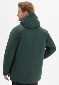 Grüne Pufferjacke mit hohem Kragen und Kapuze, ausgestattet mit einer glatten Textur und einer entspannten Passform. Rückansicht zeigt Nähte und Schulterdesign.