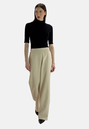 Maglione corto aderente nero a maniche corte abbinato a pantaloni beige a gamba larga; modello con tacchi a punta neri. Tessuto morbido e tonalità neutre.