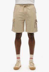 Pantaloni cargo beige con vita elasticizzata e coulisse, dotati di tasche laterali e vestibilità comoda. Realizzati in tessuto morbido, lunghezza al ginocchio.