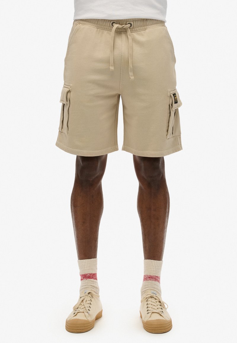 Pantaloni cargo beige con vita elasticizzata e coulisse, dotati di tasche laterali e vestibilità comoda. Realizzati in tessuto morbido, lunghezza al ginocchio.