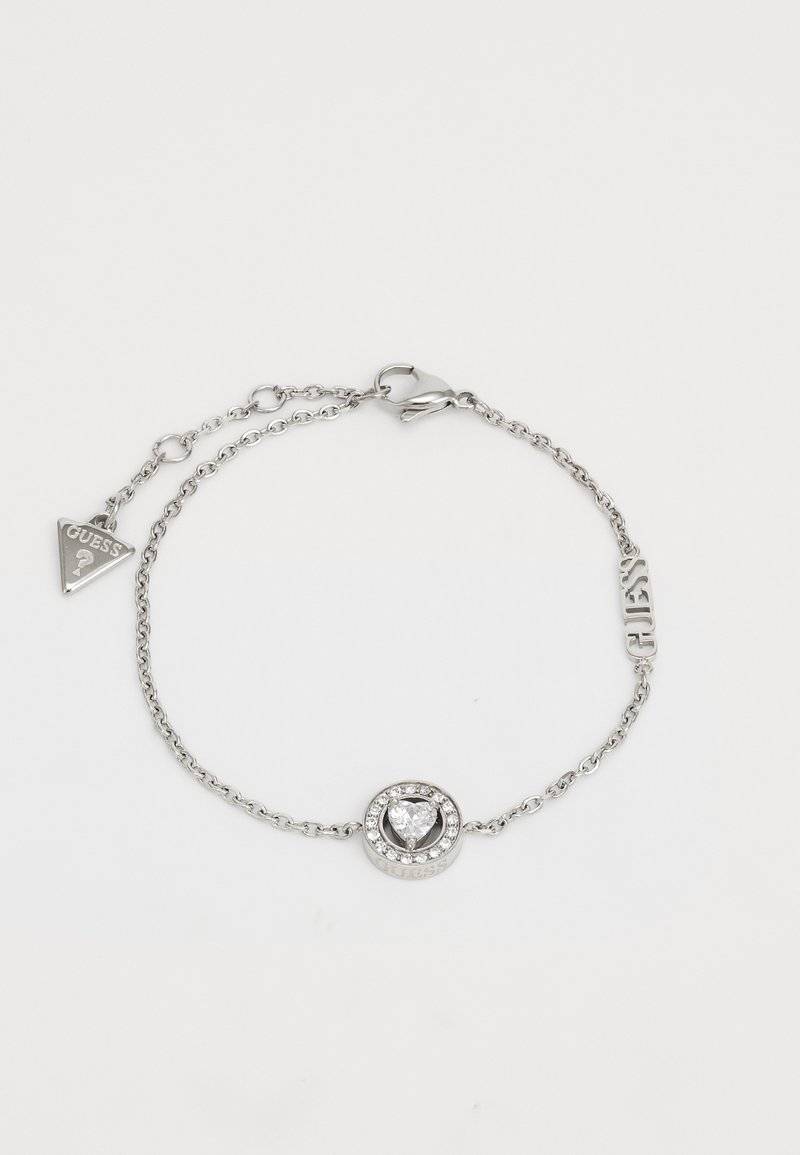 Silver chain bracelet featuring a round heart-shaped center stone surrounded by smaller clear crystals and a "GUESS" tag charm.