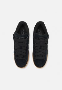 Čierne semišové tenisky s tmavými šnúrkami, gumenou podrážkou a klasickým dizajnom s tromi pruhmi. Polstrovaný interiér s logom "adidas" na jazyku.