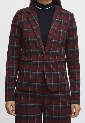 Damen-Blazer in kastanienbraunem Karomuster mit passender Hose, getragen über einem schwarzen Rollkragenpullover, das Muster zeigt grüne und schwarze Streifen.