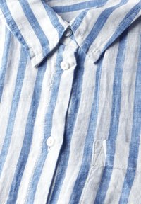 Camicia di lino con strisce verticali blu e bianche alternate, colletto alla francese, tre bottoni e taschino sul lato sinistro.