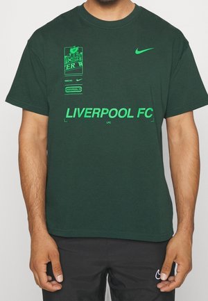 Ciemnozielona koszulka z neonowozielonym logo Nike, napisem Liverpool FC oraz graficznymi detalami na piersi, noszona przez osobę z widocznymi ramionami.