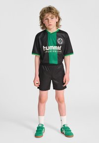Svart och grön randig sportklädesset med en kortärmad tröja och shorts, vilket har en logotyp och gröna detaljer på kragen och ärmarna.