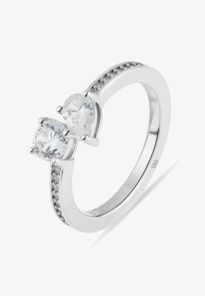 Silberner Ring mit zwei großen, klaren Edelsteinen nebeneinander, begleitet von kleineren Steinen, die entlang des Rings eingearbeitet sind.