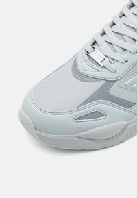 Gray athletic sneaker featuring a textured upper, smooth leather accents, and a layered design with tonal stitching and secure lacing system.