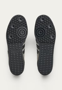Black rubber shoe sole with textured grip pattern and round accents, featuring three black stripes and an adidas logo on the side.