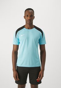 Jersey deportivo de Nike de tela azul claro con acentos negros en los hombros, combinado con pantalones cortos negros que presentan un logotipo rojo.