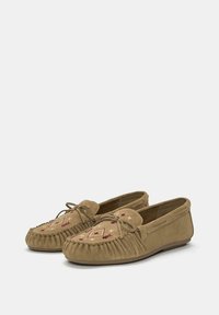 Un paio di pantofole mocassino in suede color beige con dettagli cuciti, un fiocco decorativo e motivi ricamati in bordeaux e crema sulla parte superiore.