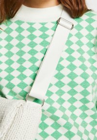 Maglione a motivi di diamante verdi e bianchi con scollo girocollo a coste, abbinato a una borsa bianca testurizzata con tracolla spessa e dettagli in metallo.