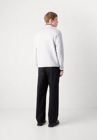 Sweatshirt gri deschis cu guler înalt, margine neagră contrastantă și pantaloni negri drepți, având o croială relaxată și o textură fină.