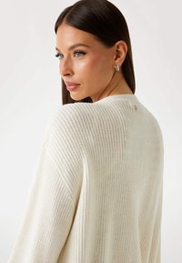 Lightweight cream knitted cardigan with a relaxed fit, featuring a textured pattern and wide sleeves, showcased from a three-quarter angle.