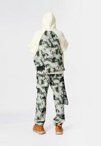 Sudadera con capucha en crema con una parte trasera texturizada y con patrón en verde y blanco. Combinada con pantalones a juego con patrón y zapatos marrón claro.