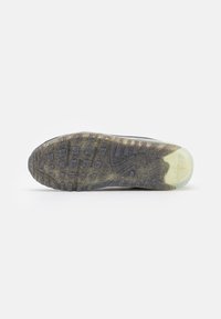 Semelle extérieure de sneaker en caoutchouc noir texturé, avec un accent translucide au talon et un motif de bande de roulement pour l'adhérence. Marques de saleté visibles.