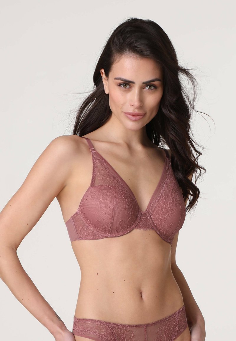 Reggiseno in pizzo rosa tenue con coppe imbottite e spalline larghe. Presenta una sovrapposizione in pizzo floreale e tessuto liscio, progettato per comfort e sostegno.