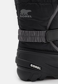 Bota negra impermeable con parte superior de nylon texturizado, banda elástica gris, logo de Sorel y suela de goma resistente para tracción.