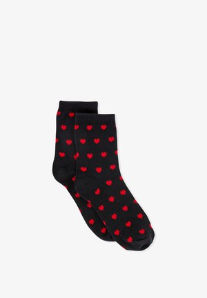 Ein Paar schwarze Socken mit verstreuten kleinen roten Herzmustern, knöchellang, flach auf weißem Hintergrund.