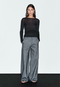 Black sheer long-sleeve top paired with grey, high-waisted wide-leg trousers featuring a subtle pinstripe pattern. Smooth texture, modern fit.