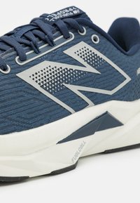 Chaussure de sport marine avec un dessus en tissu texturé, détail de logo blanc, talon renforcé et semelle intercalaire matelassée blanche et grise.
