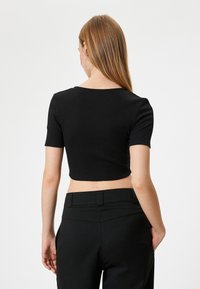 Sort ribbet crop top med korte ærmer, rund halsudskæring og tætsiddende design, parret med højtaljede sorte bukser.