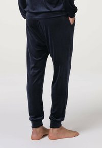 Pantaloni jogger navy in morbido tessuto peluche. Presentano polsini alle caviglie e tasche laterali. Texture liscia con una vestibilità comoda.