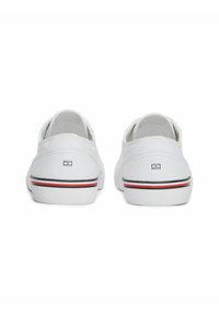 Zapatillas de lona blancas con un diseño de caña baja, que cuentan con una suela de goma y una delgada línea negra y roja en la parte inferior. Logo en la parte trasera.