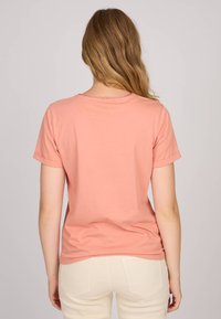 T-shirt à manches courtes, de couleur rose doux, avec un col rond et des manches retroussées, fabriqué en tissu léger, présenté de dos.