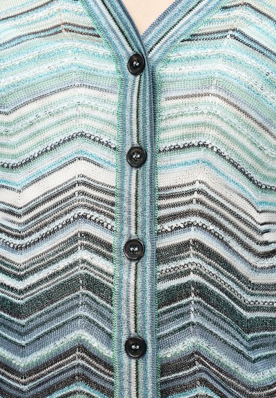 Πλεκτή ζακέτα με σχέδιο ζιγκ-ζαγκ σε τιρκουάζ, πράσινο και μαύρο. Πέντε μαύρα κουμπιά κατά μήκος του μπροστινού μέρους, με ριμπ κορδόνι στο γιακά.